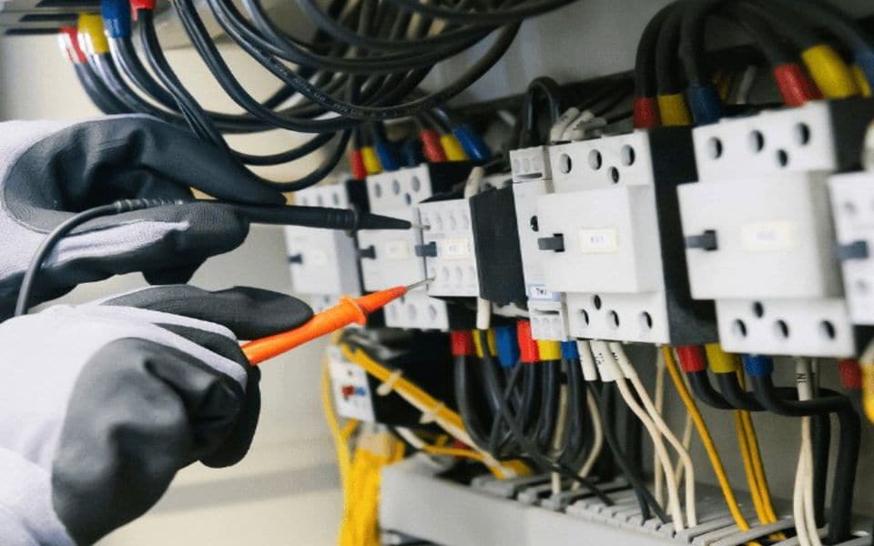 An engineer testing an electrical panel with a digital multimeter during preventive maintenance
