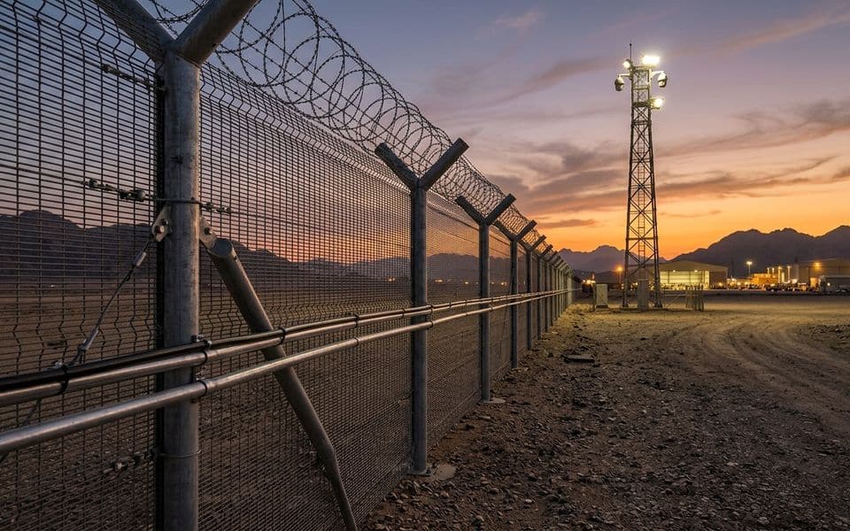 Security fence with razor wire and a watch tower at sunset